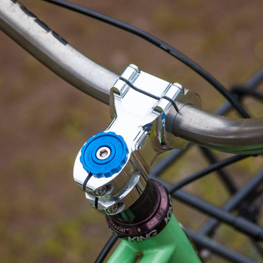 Close-up of a bicycle handlebar with a blue clamp and silver hardware against a blurred natural background.