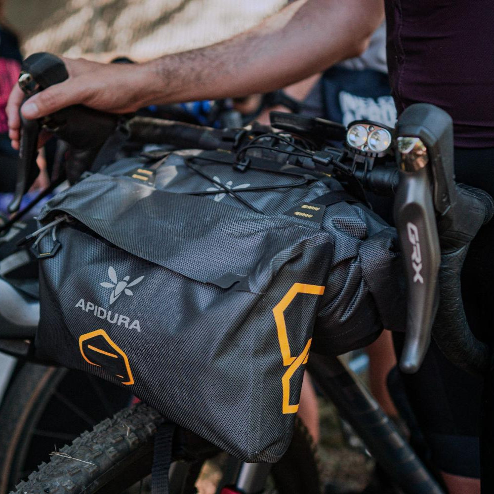 Person adjusting a bikepacking bag on a bicycle with Apidura branding.