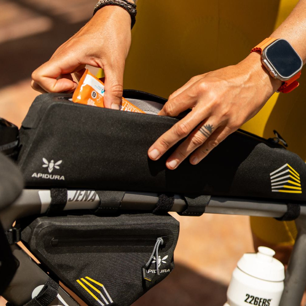 Person organizing items in a black Apidura bag on a bicycle.