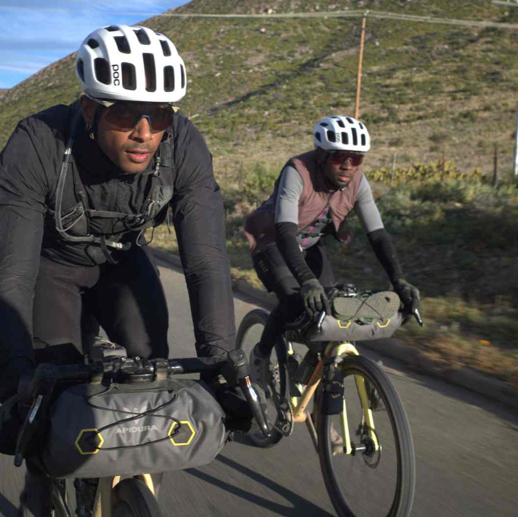 Two cyclists on a road with mountains in the background