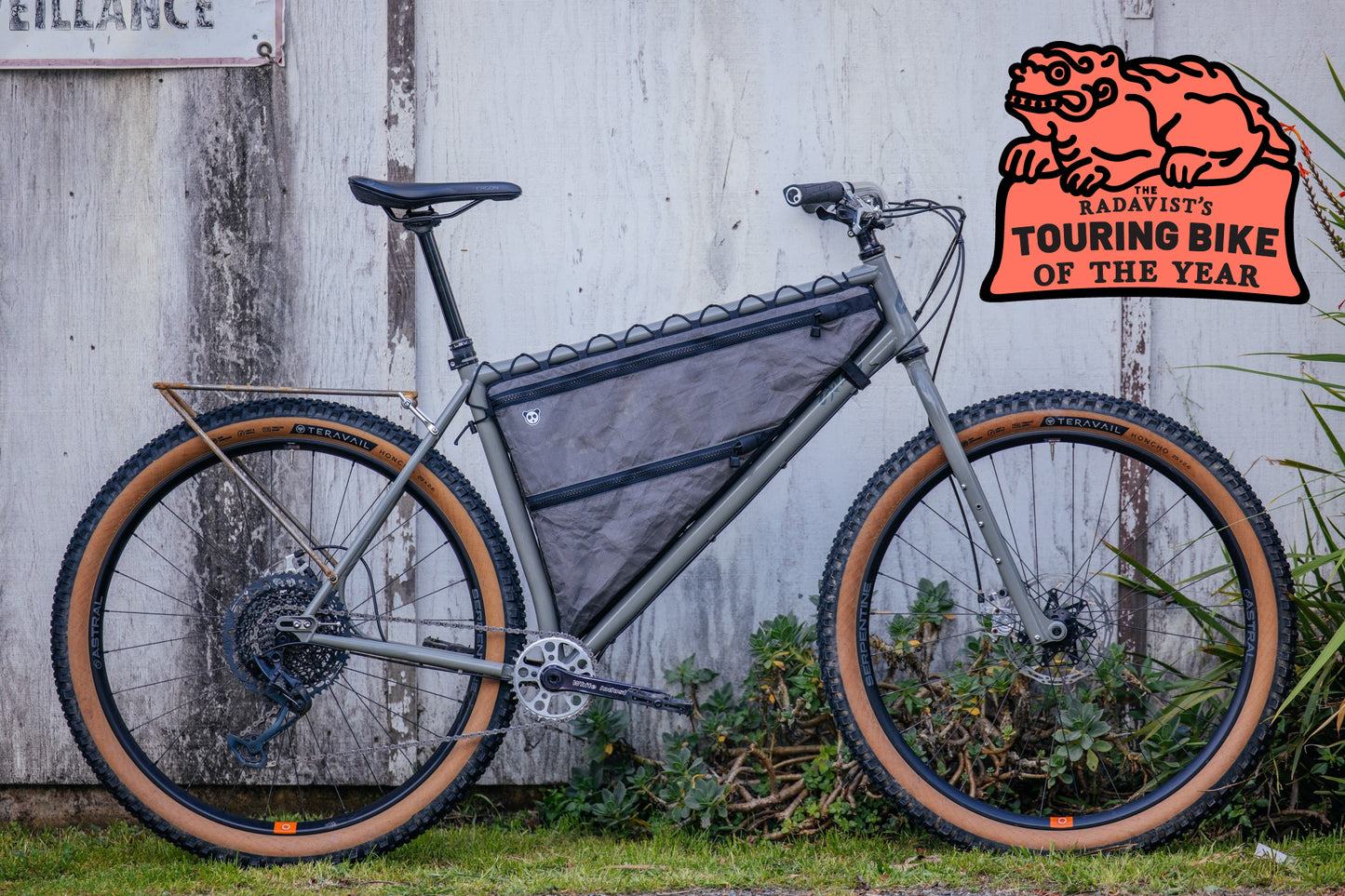 Bicycle with a bag attached, leaning against a wooden wall with a logo in the corner.