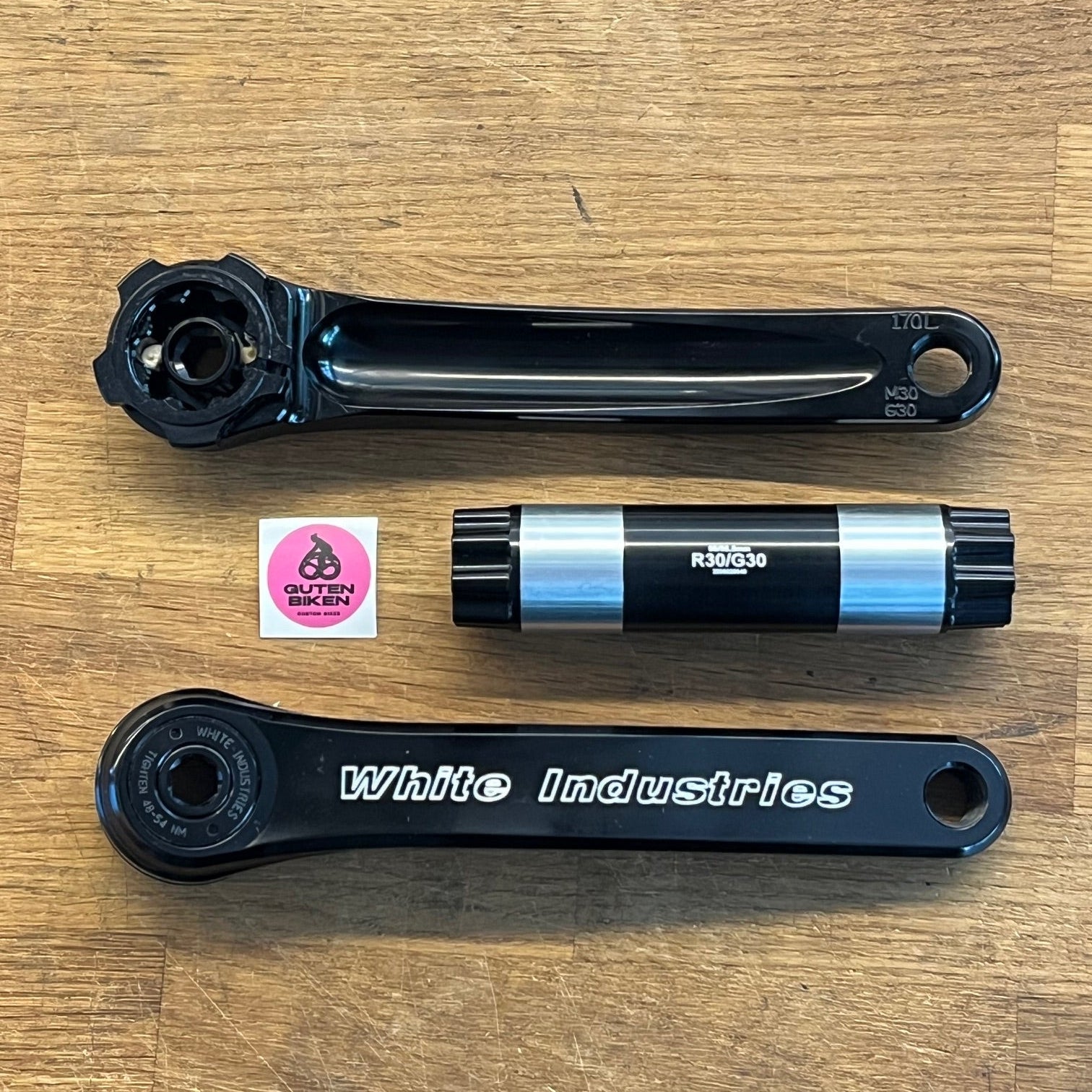 Bicycle crankset components on a wooden surface with a visible brand sticker.