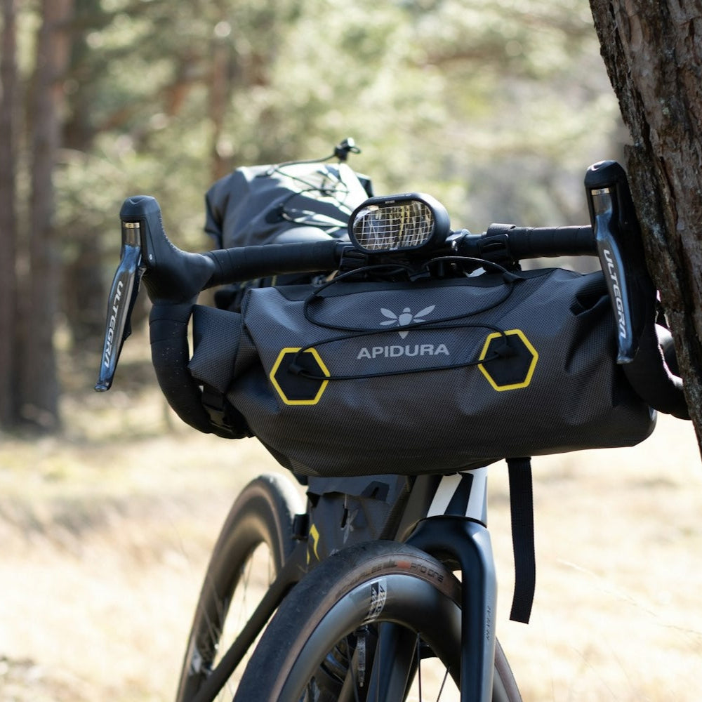 Bicycle with Apidura bags parked against a tree in a forest setting
